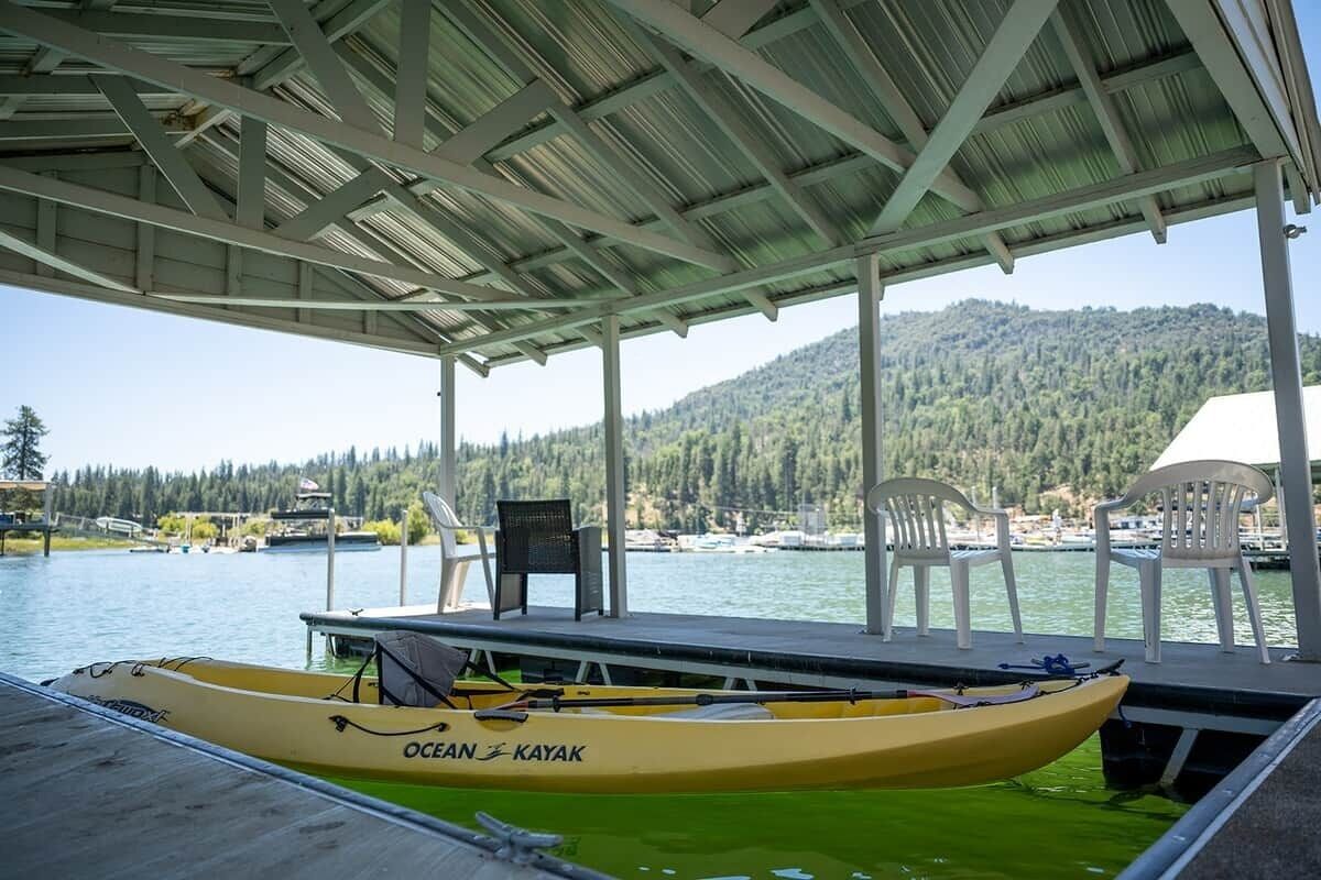 Un muelle cubierto con un kayak, sillas y vistas a un lago y colinas boscosas.