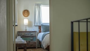Un dormitorio con cama, mesita de noche, lámpara y ventana con cortinas.