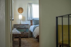 Ein Schlafzimmer mit einem Bett, einem Nachttisch, einer Lampe und einem Fenster mit Vorhängen.