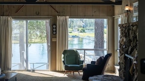 Habitación con un ventanal grande con vista a una masa de agua, un sillón verde, un sillón negro y una pared de piedra.