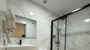 A modern bathroom with a marble backsplash, a white sink, a toilet, and a glass-enclosed shower.