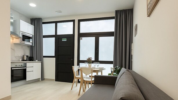 A modern living room with a large sofa, a dining area with a table and chairs, and a kitchen with a microwave and oven.