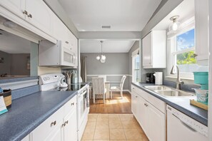 A modern kitchen with white cabinetry, a built-in oven, a dining area with a table and chairs, and a window providing natural light.
