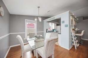 A modern kitchen with a glass dining table, white chairs, and a hanging light fixture.