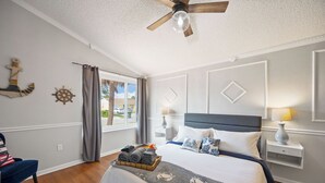 A neatly arranged bedroom with a bed, bedside tables, a ceiling fan, and a window with curtains.