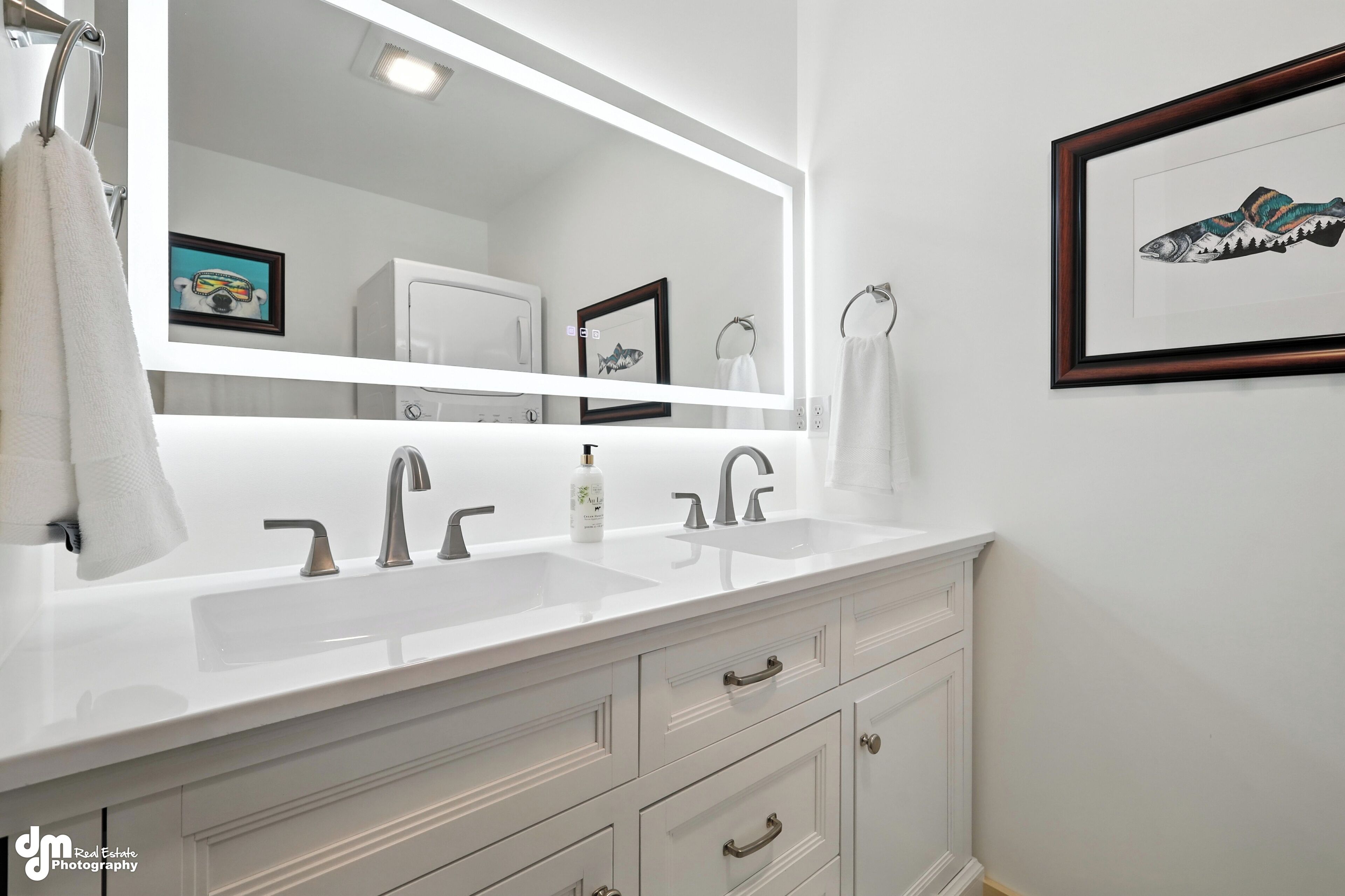 Un baño moderno con tocador blanco, dos lavamanos y un espejo grande.