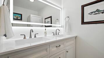 Un baño moderno con tocador blanco, dos lavamanos y un espejo grande.