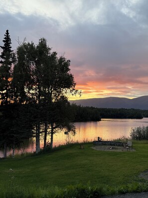 A lakeside view with a grassy area, trees, and a stone bench. - Peaceful with views, brand new, 2-bedroom, 2 bathroom house on Finger Lake. (Palmer)