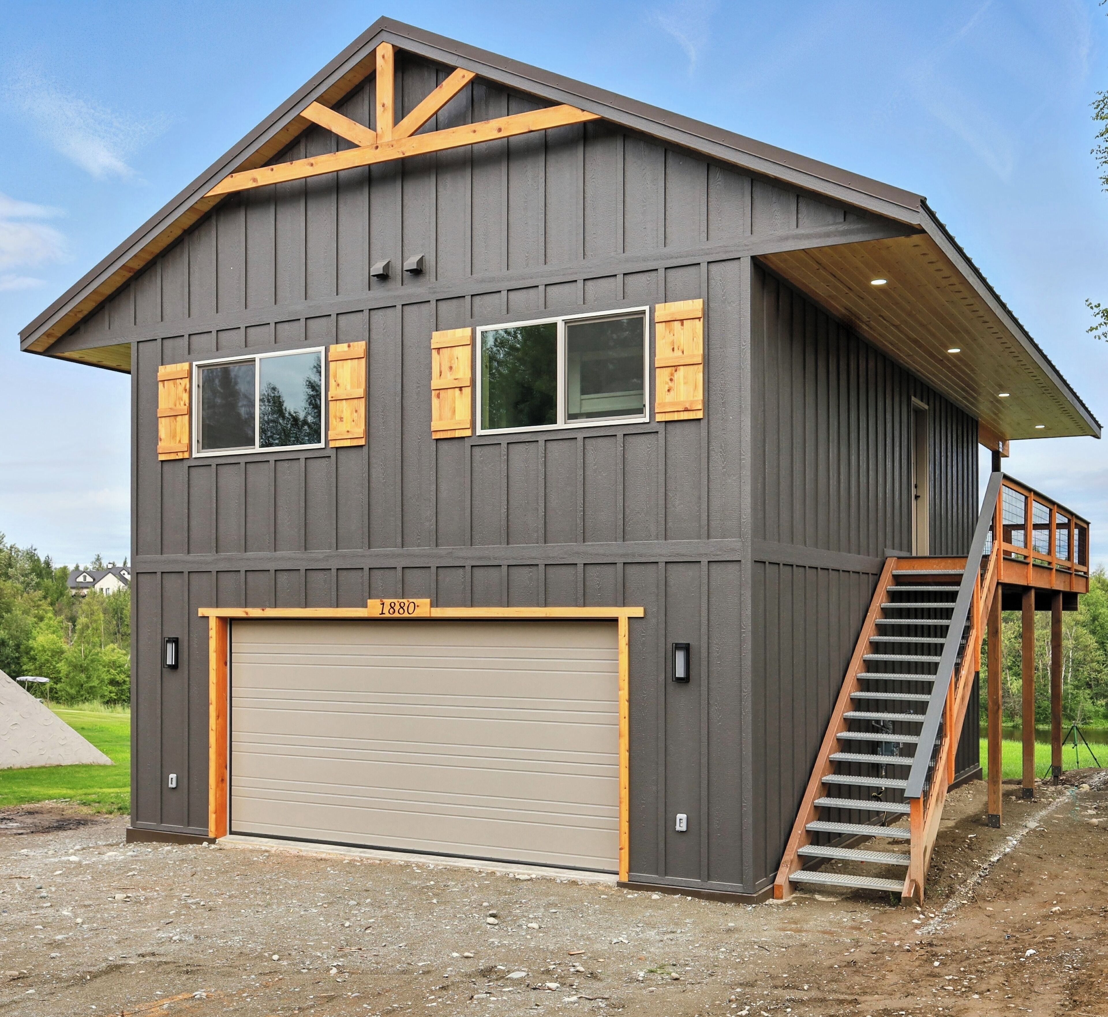 A modern two-story house with a large garage, wooden shutters, and a wooden staircase leading to an upper level.