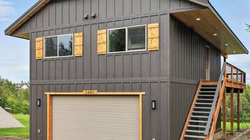 A modern two-story house with a large garage, wooden shutters, and a wooden staircase leading to an upper level.