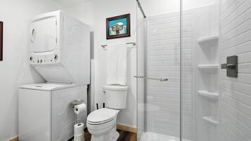 A modern bathroom with a built-in washer and dryer, a toilet, and a glass-enclosed shower.