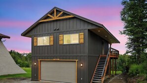 A two-story building with a garage door, a wooden staircase, and a balcony. - Peaceful with views, brand new, 2-bedroom, 2 bathroom house on Finger Lake. (Palmer)