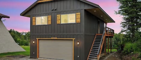 A two-story building with a garage door, a wooden staircase, and a balcony.