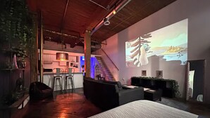 A modern living room with a large bed, a kitchen area, and a staircase.