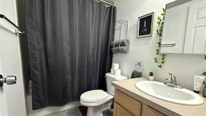 A bathroom with a shower curtain, toilet, sink, and cabinets.