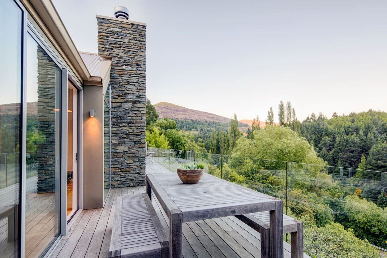 Eine moderne Terrasse im Freien mit einer Steinwand, einem Holztisch und einem Blumentopf.