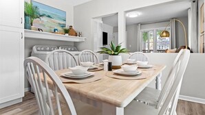 A modern kitchen with white cabinetry, a wooden dining table set with plates and a potted plant. - Cozy 3BR Getaway with Hot Tub, Firepit & BBQ (Clinton Township)