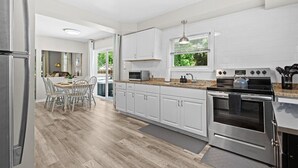 A modern kitchen with white cabinetry, a granite countertop, stainless steel appliances, and a dining area with a wooden table and chairs. - Cozy 3BR Getaway with Hot Tub, Firepit & BBQ (Clinton Township)