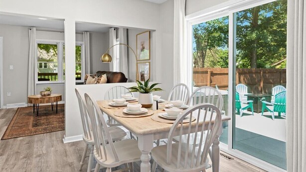 A dining area with a wooden table set for six, white chairs, and a view of the backyard through large sliding glass doors. - Cozy 3BR Getaway with Hot Tub, Firepit & BBQ (Clinton Township)