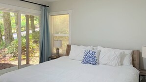 A bedroom with a large bed, a nightstand, a lamp, and a window with curtains. - Sudden Valley Retreat 3BR House -Steps to Lake Louise (Bellingham)