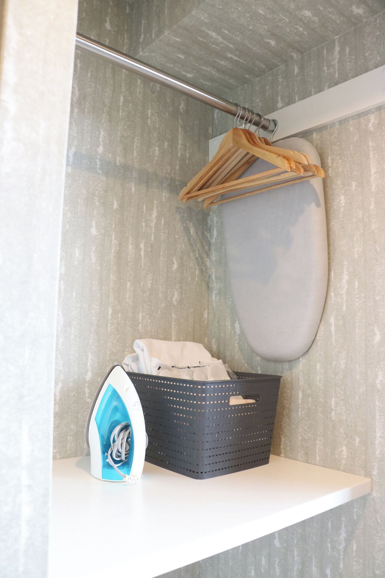 A laundry area with a hanging rack, a basket with clothes, and an iron.