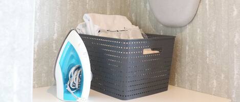 A laundry area with a hanging rack, a basket with clothes, and an iron.