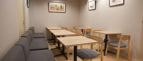A dining area with long tables and benches, framed artwork on the walls, and a wooden floor.