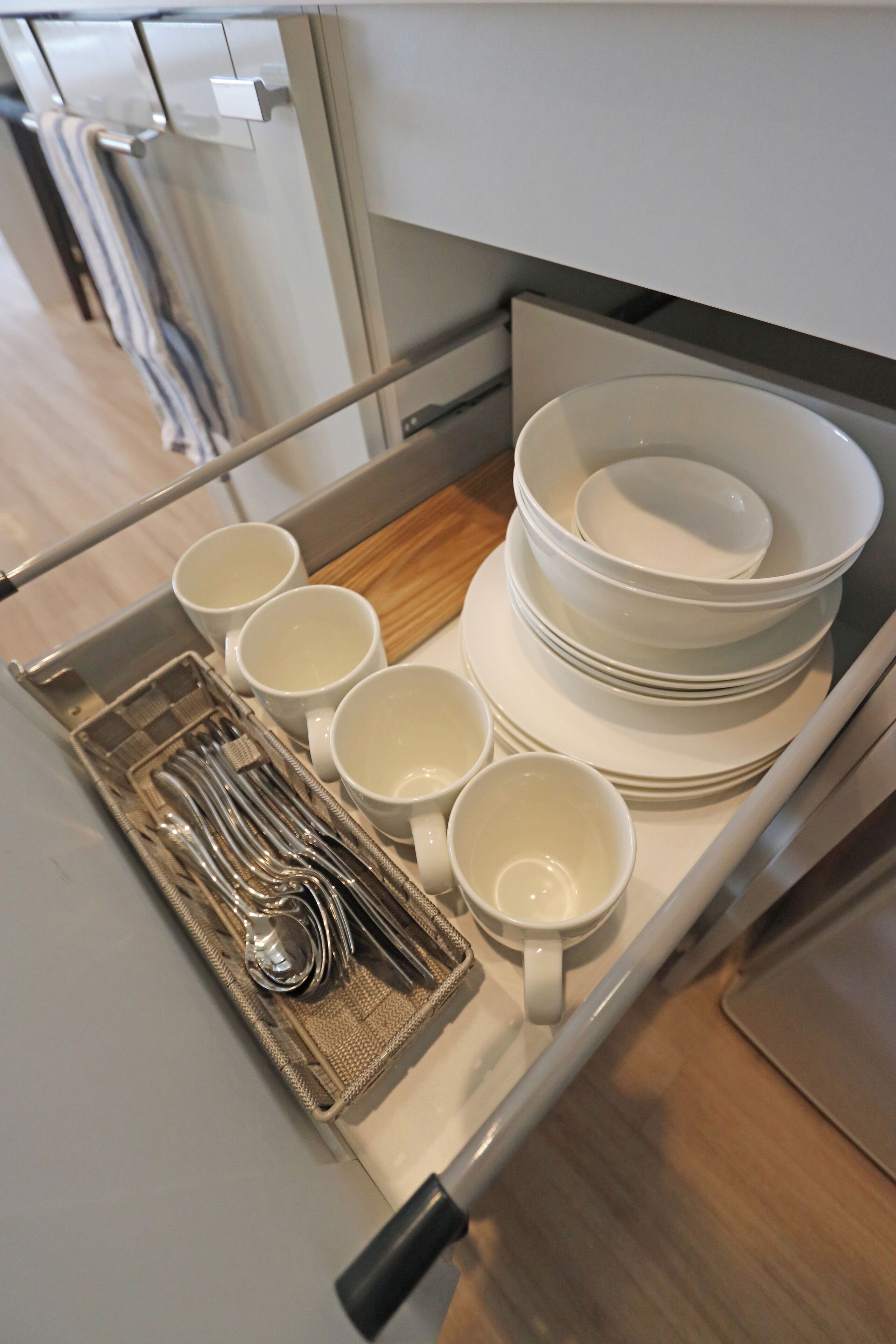 A kitchen with a built-in utensil holder containing a set of silverware, multiple white mugs, and stacked white plates.
