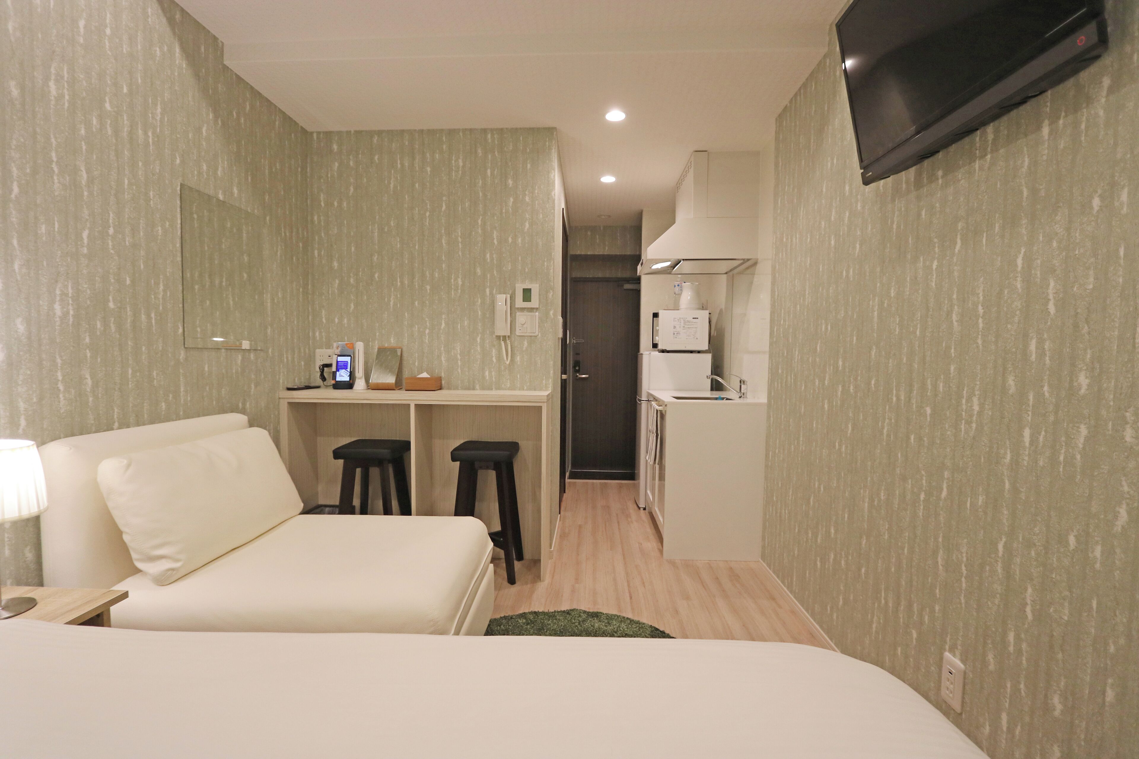 Una habitación de hotel con cama, un escritorio con computadora, televisión y kitchenette.