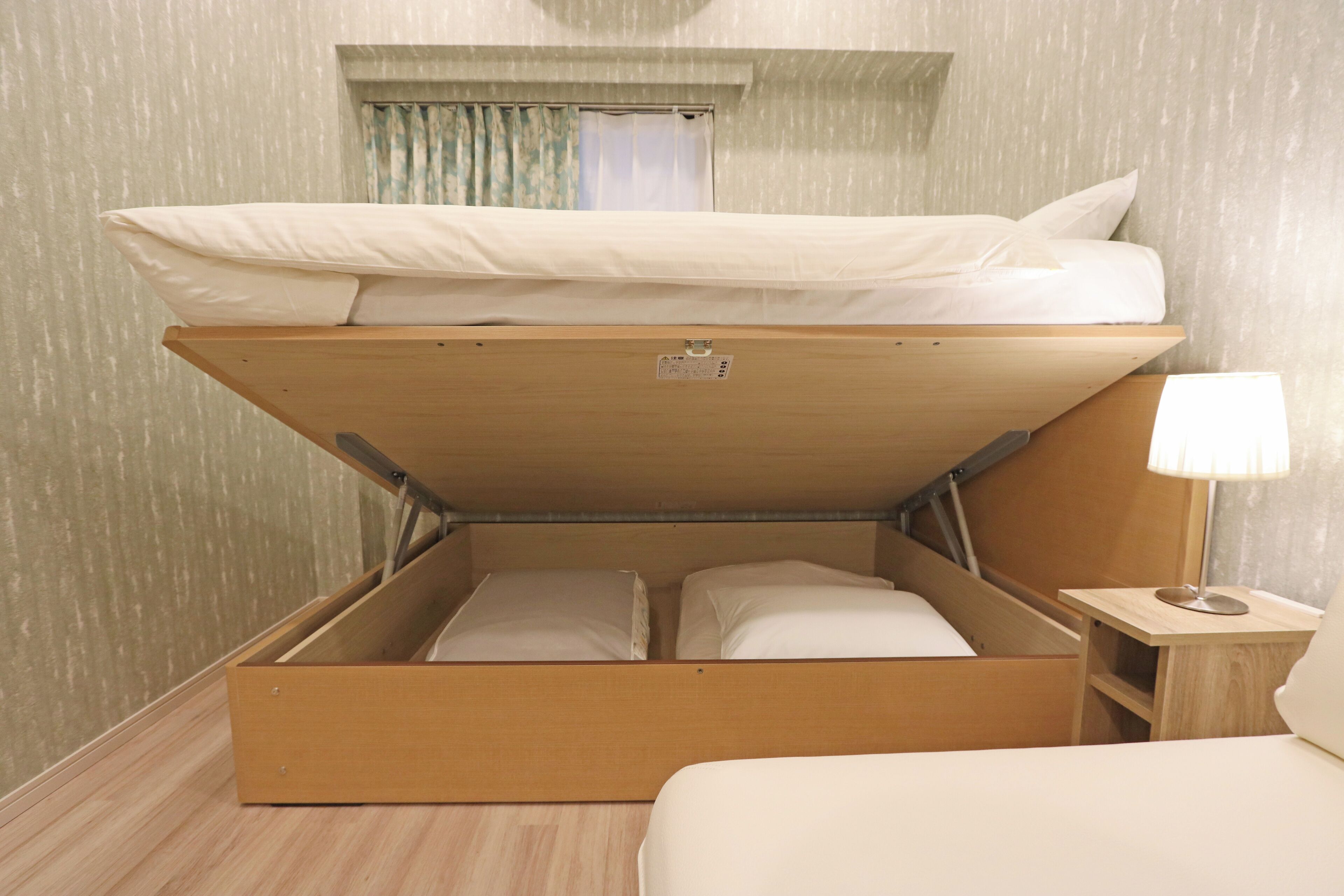 A compact room with a bunk bed, a small bedside table with a lamp, and a window with curtains.