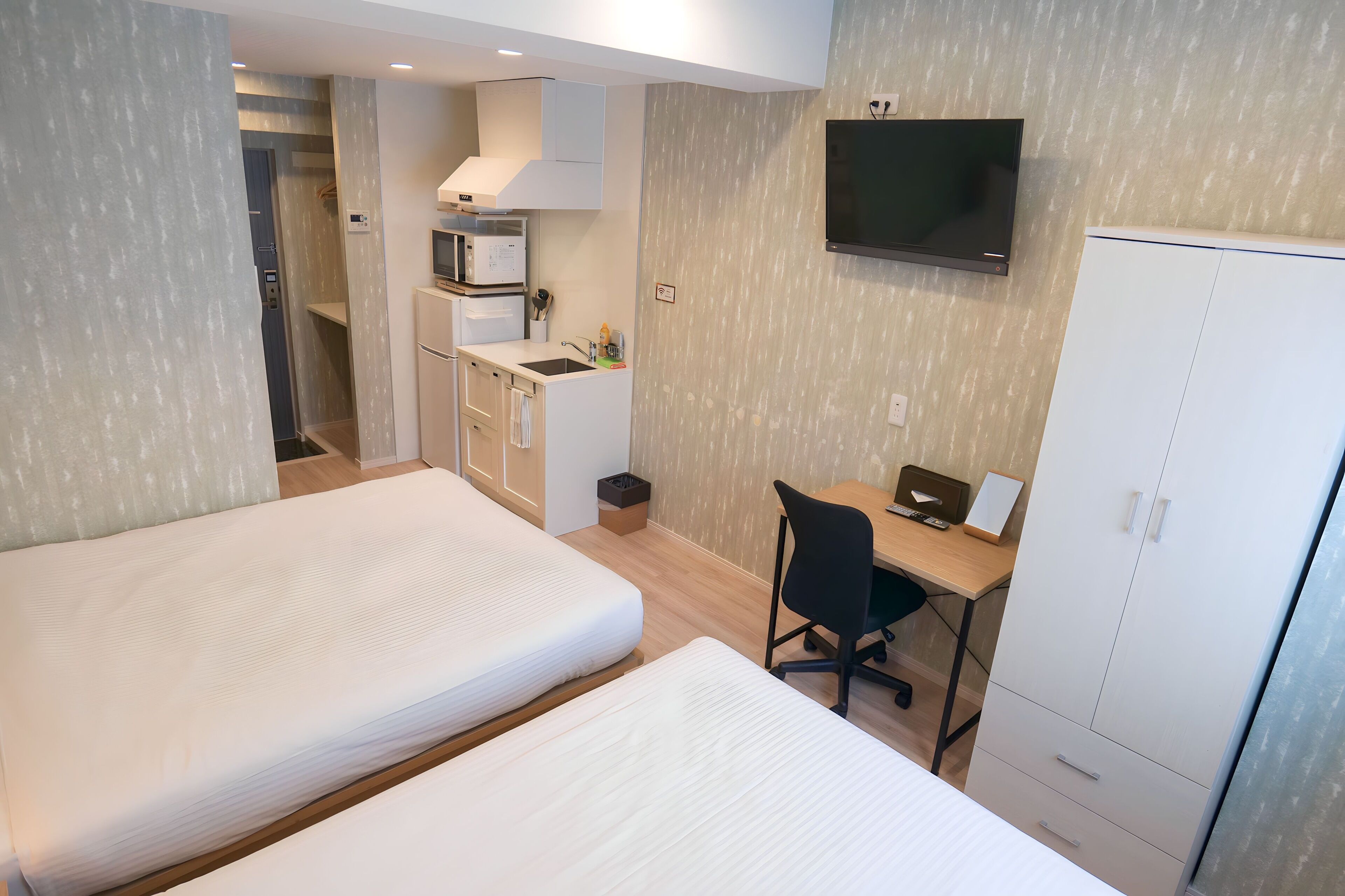 Et hotelværelse med to senge, et tekøkken, et fjernsyn og et skab.