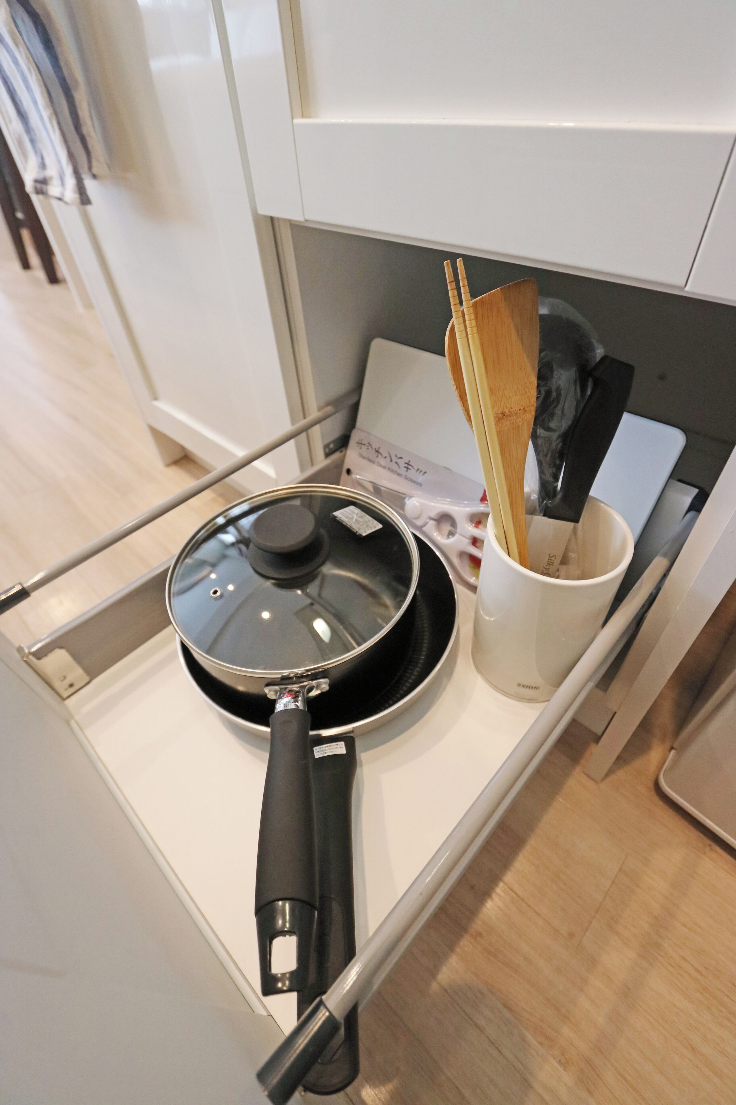 A kitchen counter with a frying pan, a white mug with chopsticks and a spatula, and a white appliance.