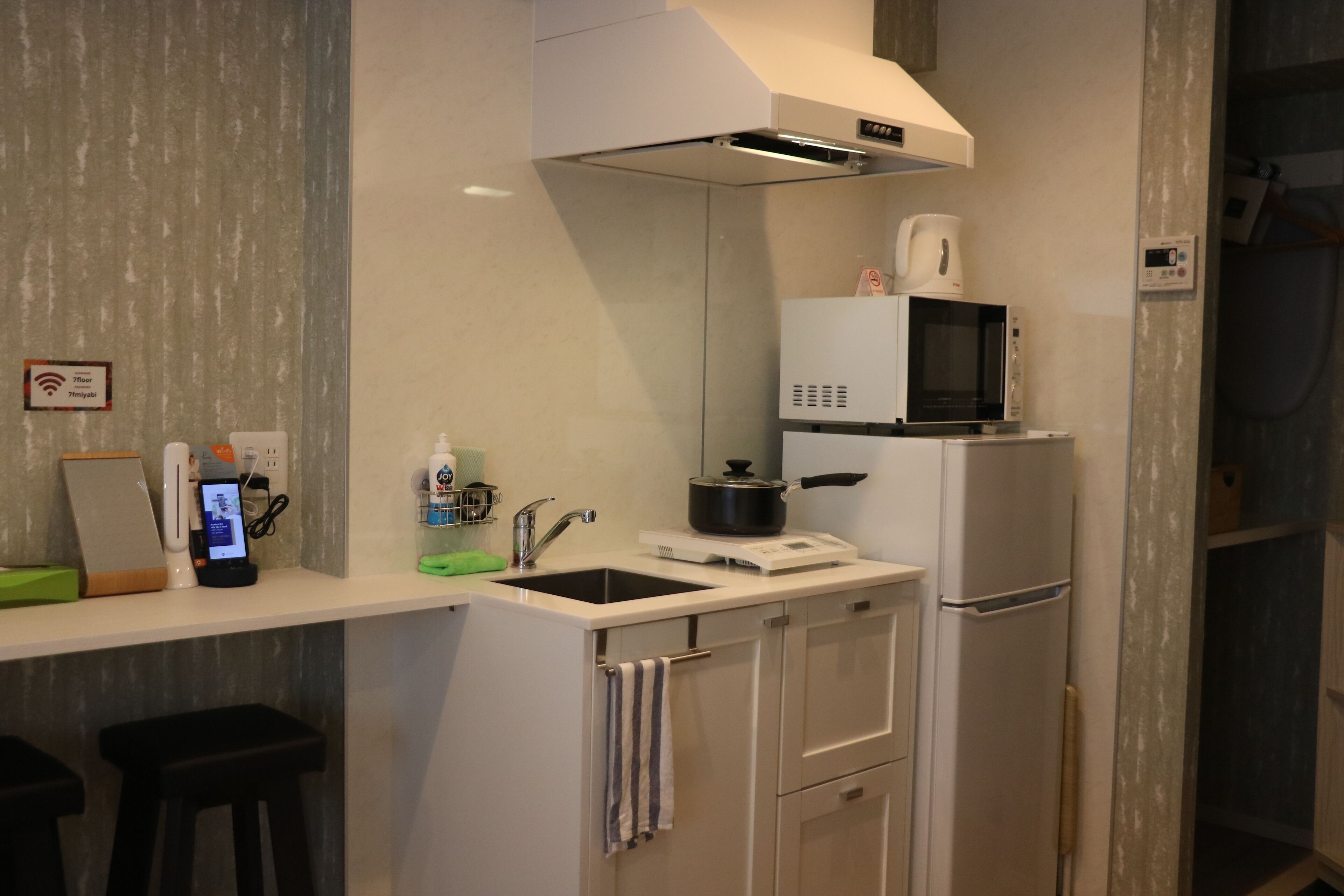 A modern kitchen with a microwave, stove, and sink. There is a small bar area with stools and a digital payment terminal.