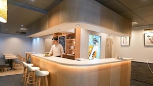 Zona de bar moderna amb un taulell corbat, tamborets de fusta, i una persona al darrere.
