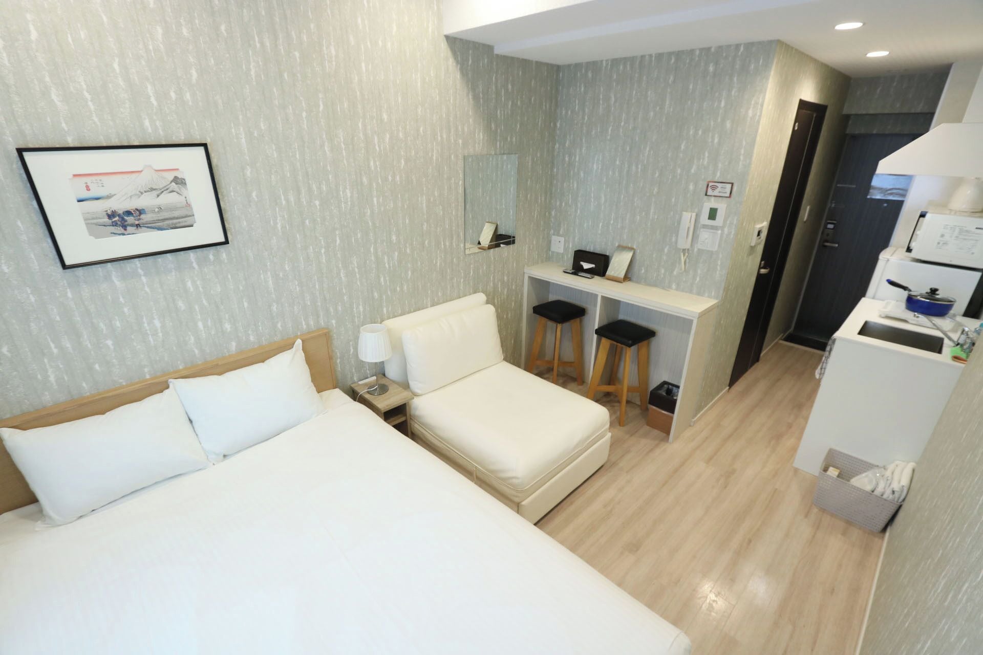 Ein Hotelzimmer mit zwei Betten, einem Schreibtisch mit zwei Hocker, einem Spiegel und einer Küchenzeile.