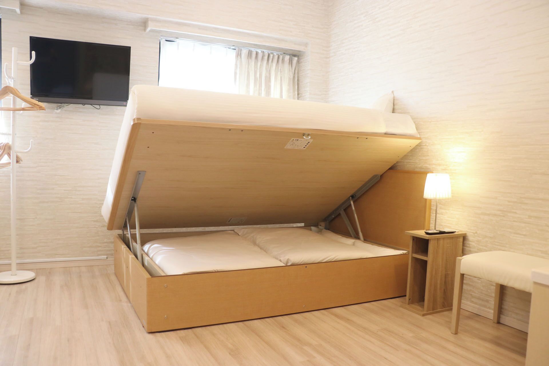 Habitación compacta con una cama plegable, una mesita de noche pequeña con lámpara y un televisor montado en la pared.