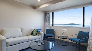Ein modernes Hotelzimmer mit einer Sitzecke, zwei Sesseln, einem Couchtisch und Meerblick.