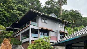Une maison à deux étages avec une piscine, entourée d’une végétation luxuriante et d’un mur de pierre.