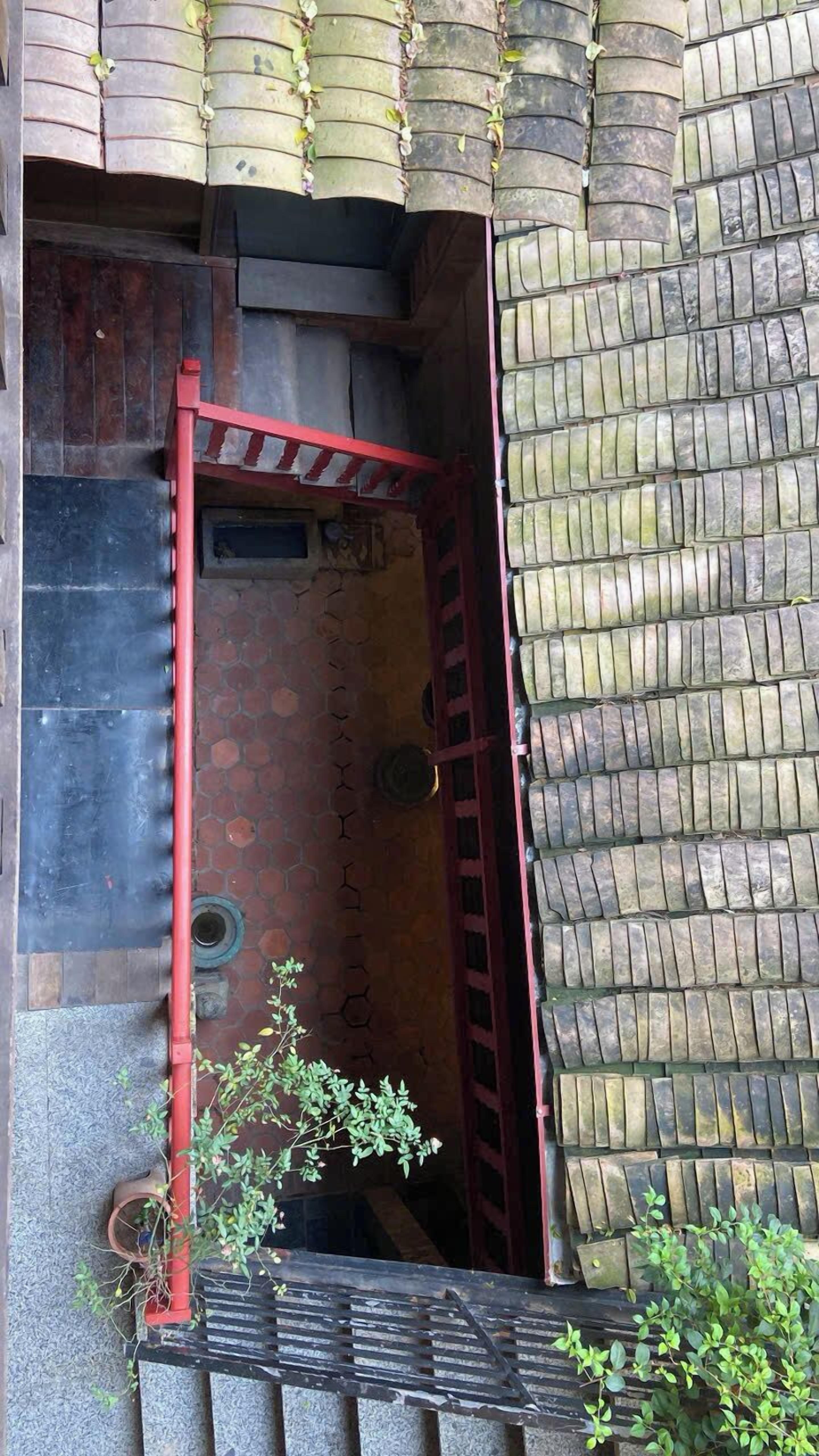 Una escalera estrecha y cerrada con barandilla roja que lleva a una puerta.