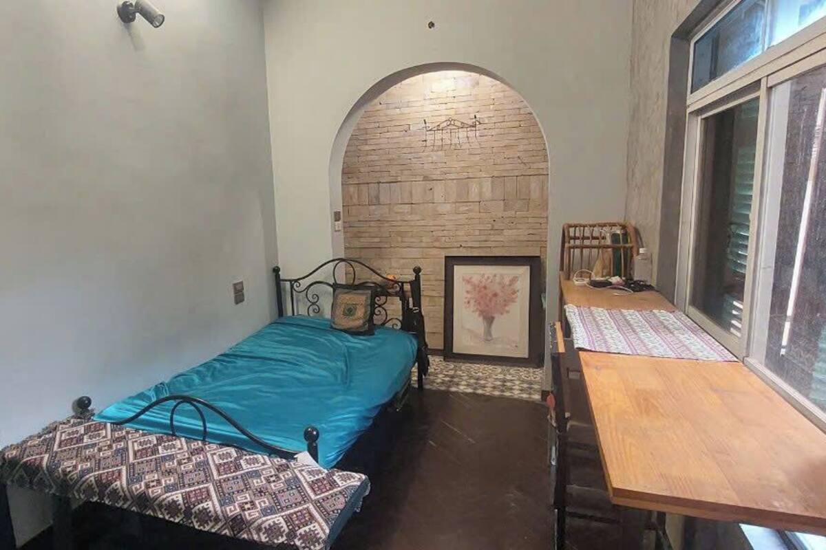 Un dormitorio pequeño con una cama, una mesa de madera, un ventanal y un adorno en la pared.