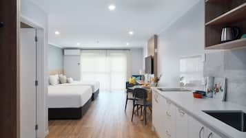 Une chambre d’hôtel moderne comprenant un lit, un bureau avec une chaise, un petit coin cuisine et une salle de bain visible à travers une porte ouverte.