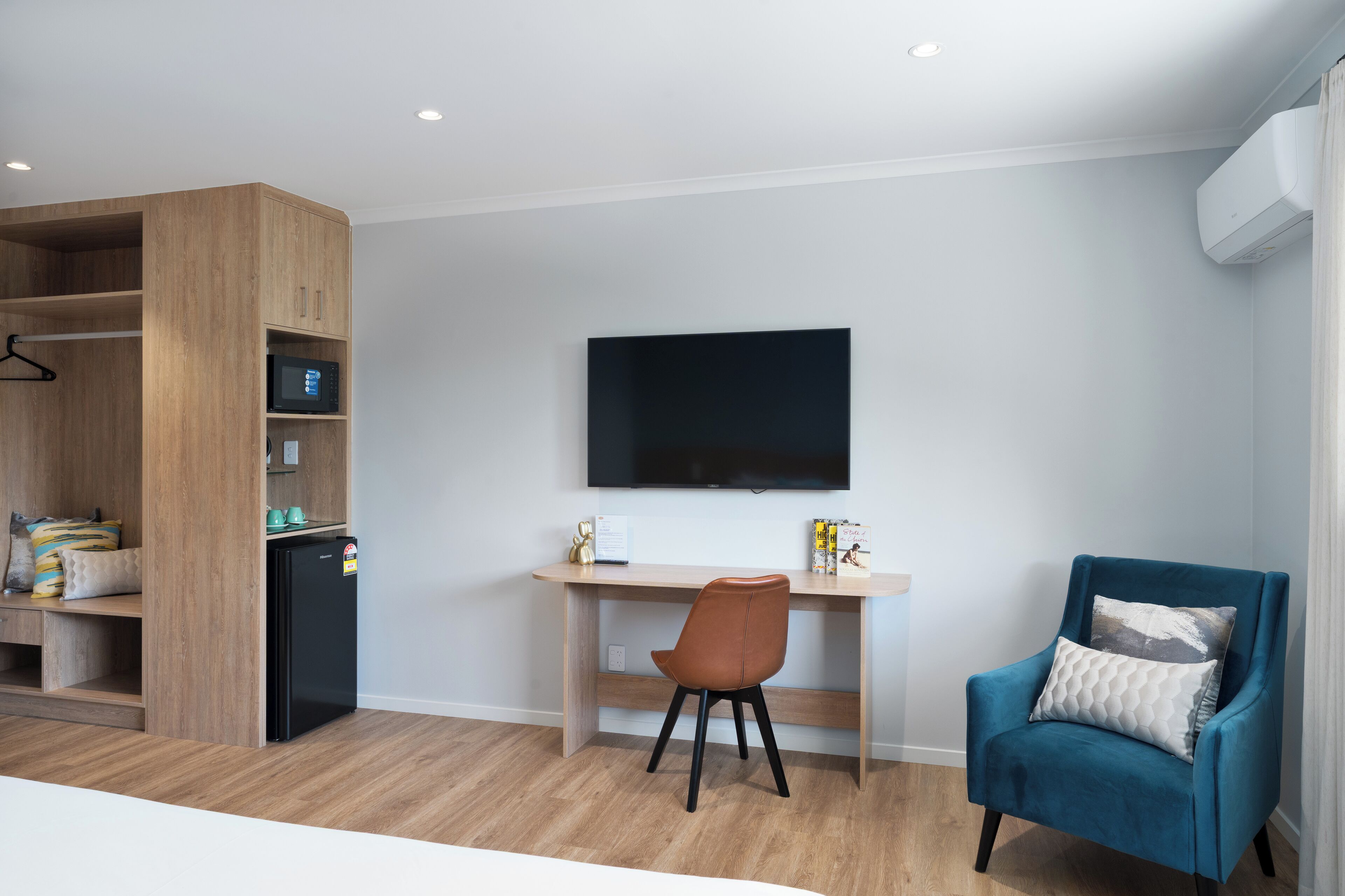 Habitación moderna con un armario de madera, un escritorio con computadora, un sillón azul y un televisor montado.