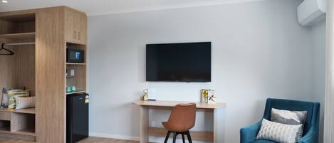 Habitación moderna con un armario de madera, un escritorio con computadora, un sillón azul y un televisor montado.