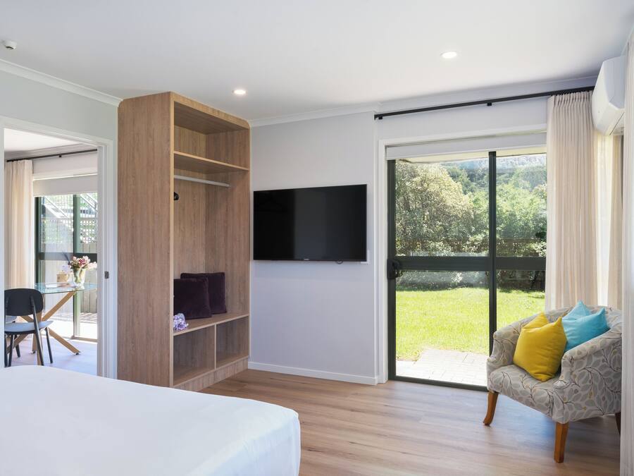 Un dormitorio moderno con una cama grande, un televisor montado en la pared y un ventanal corredero que da a un balcón.