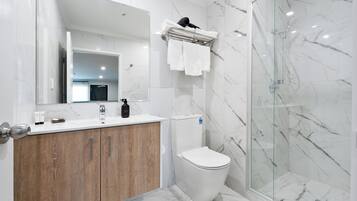 Un baño moderno con ducha de mármol, tocador de madera, inodoro y un espejo grande.