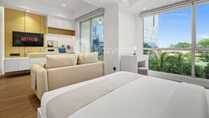 Una habitación de hotel moderna con una cama grande, una televisión mostrando 'NETFLIX', un sofá, una mesita y una ventana con vistas a la ciudad.