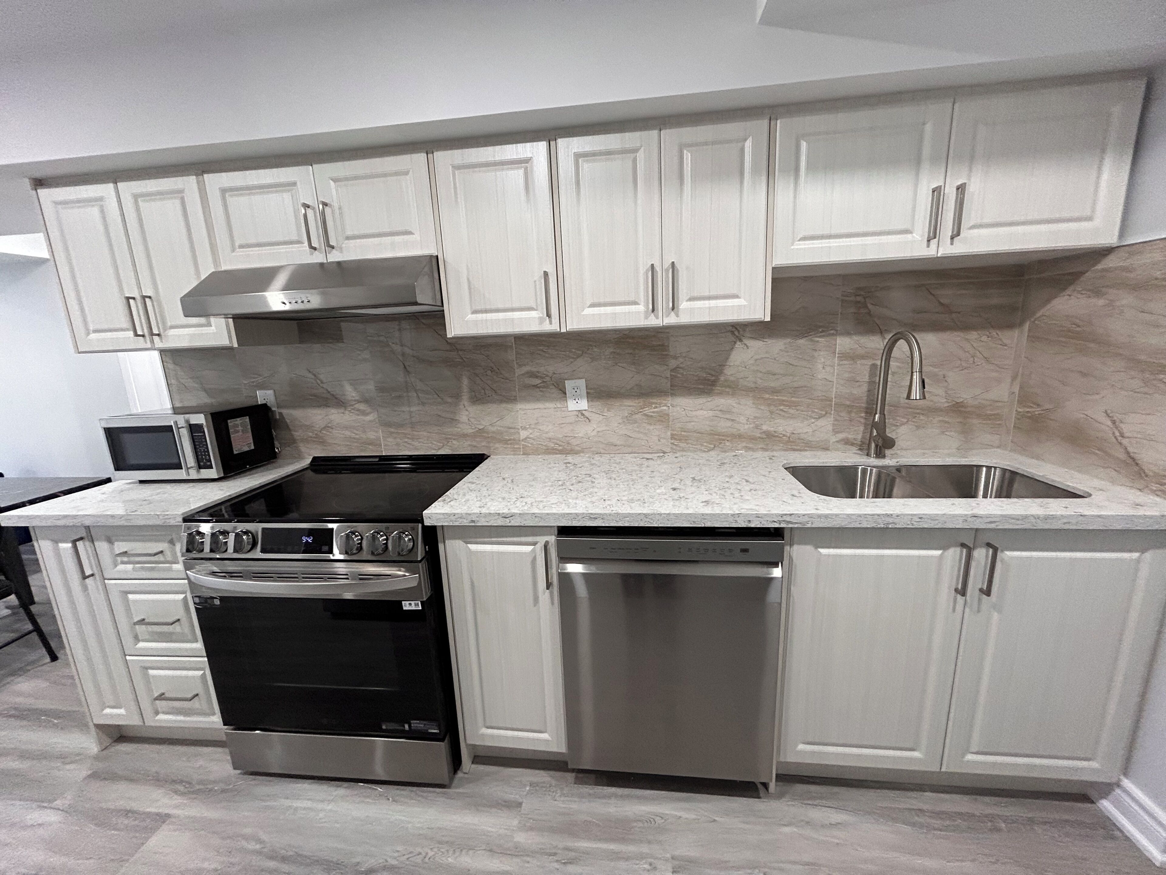 A modern kitchen with white cabinetry, a stainless steel dishwasher, a built-in oven, and a microwave.