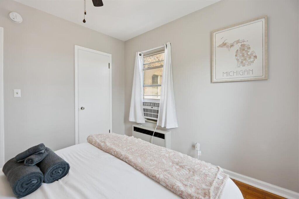 Een slaapkamer met een bed, een raam met gordijnen, een wandairconditioner en een inlijstte kaart van Michigan.