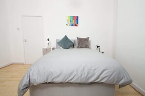 A bedroom with a bed, a nightstand, a lamp, and a colorful artwork on the wall. - Cosy 2BR Flat Near Anfield & Goodison, Liverpool (Liverpool)