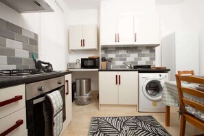 A compact kitchen with a stove, microwave, washing machine, and cabinets. - Cosy 2BR Flat Near Anfield & Goodison, Liverpool (Liverpool)